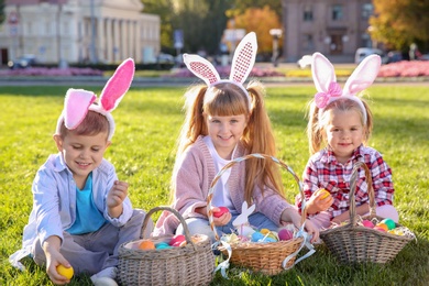 Cute little children with bunny ears and baskets of Easter eggs in park