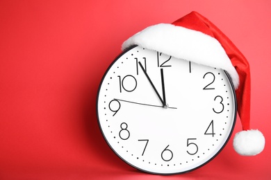 Photo of Clock with Santa hat showing five minutes until midnight on red background, space for text. New Year countdown