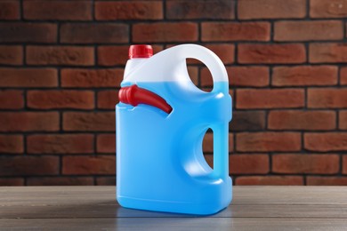 Plastic canister with blue liquid on wooden table against brick wall