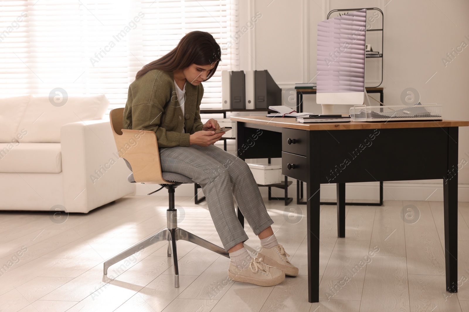 Photo of Young woman with bad posture using smartphone in office