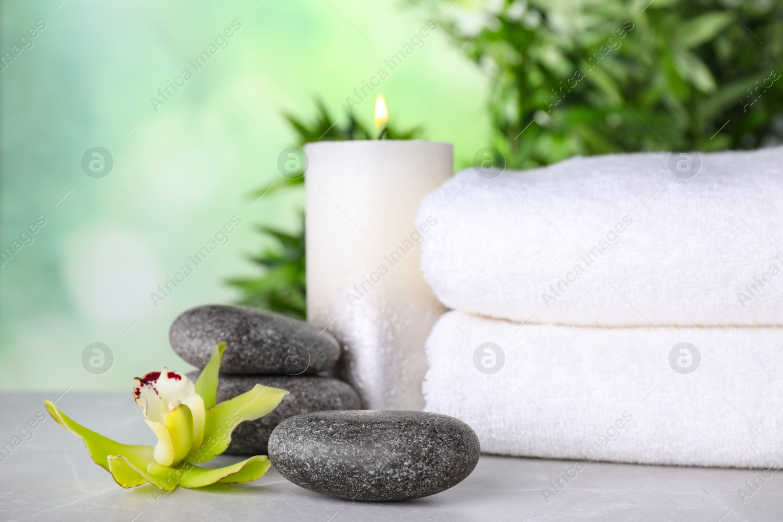 Photo of Exotic flower, spa stones, candle and towels on grey table against blurred green background, space for text
