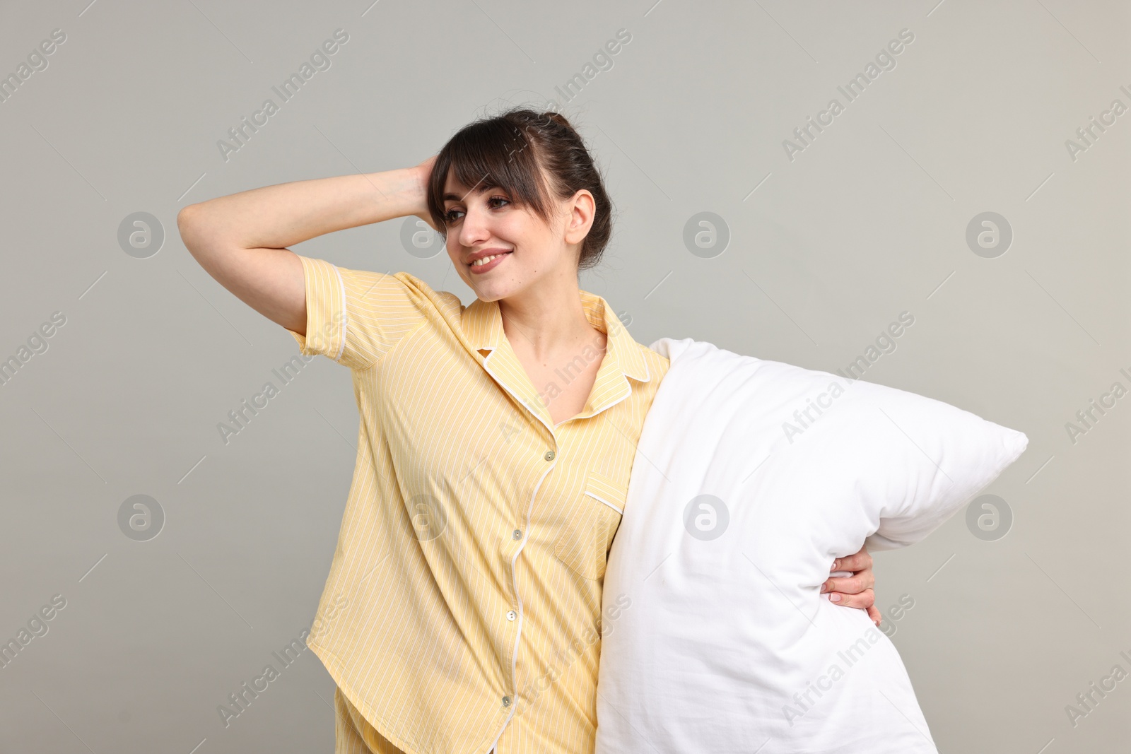 Photo of Happy woman in pyjama holding pillow on grey background