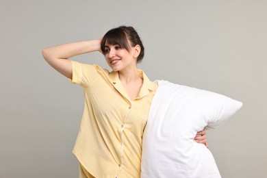 Happy woman in pyjama holding pillow on grey background