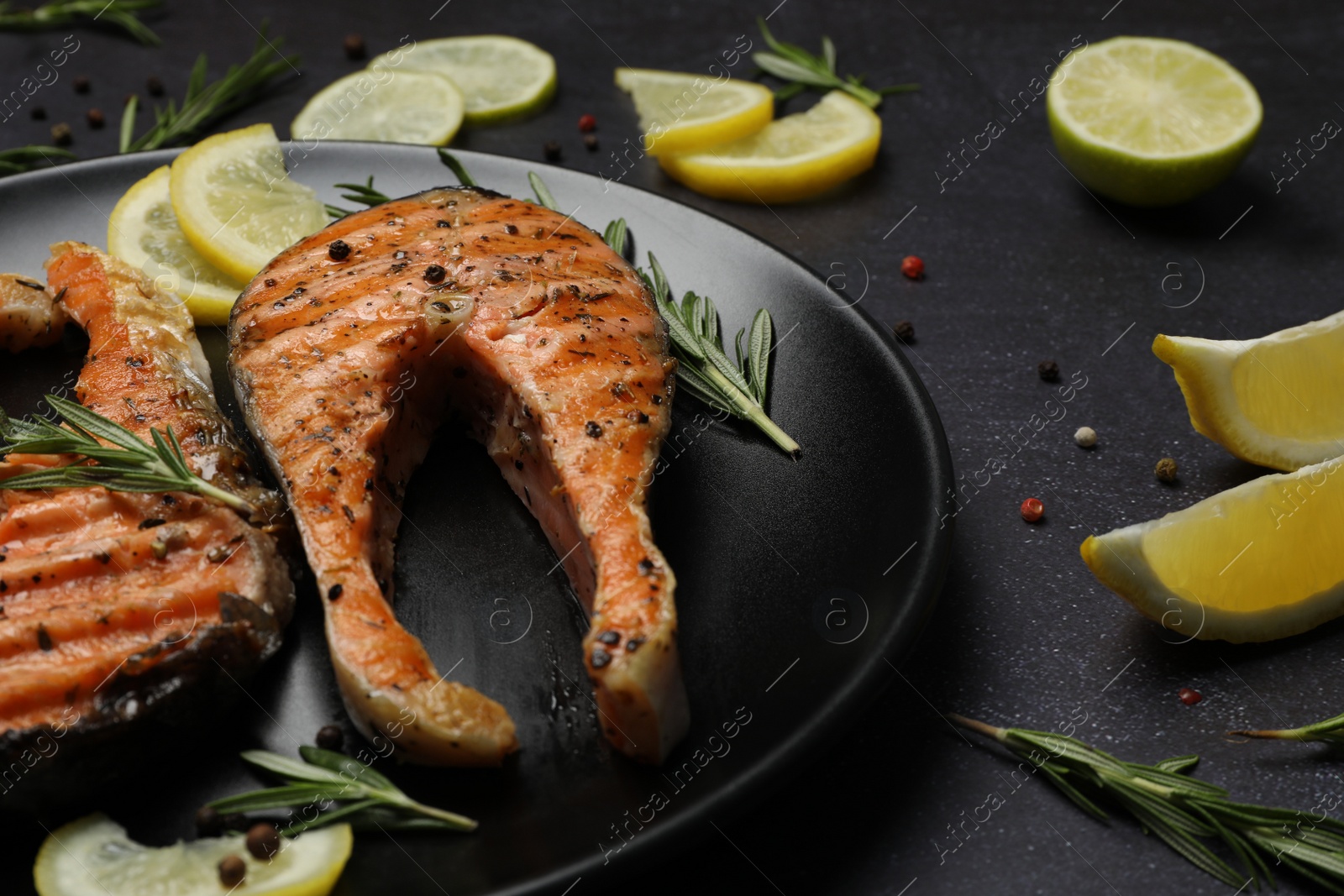 Photo of Plate with tasty salmon steaks on black table, closeup