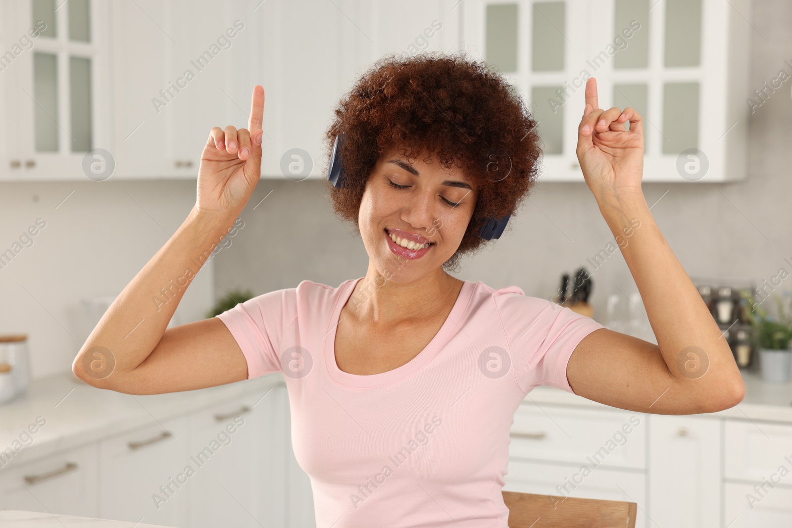 Photo of Beautiful young woman with headphones enjoying music in kitchen