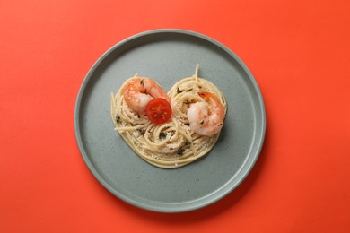 Photo of Heart made of tasty spaghetti, tomato, shrimps and cheese on coral background, top view