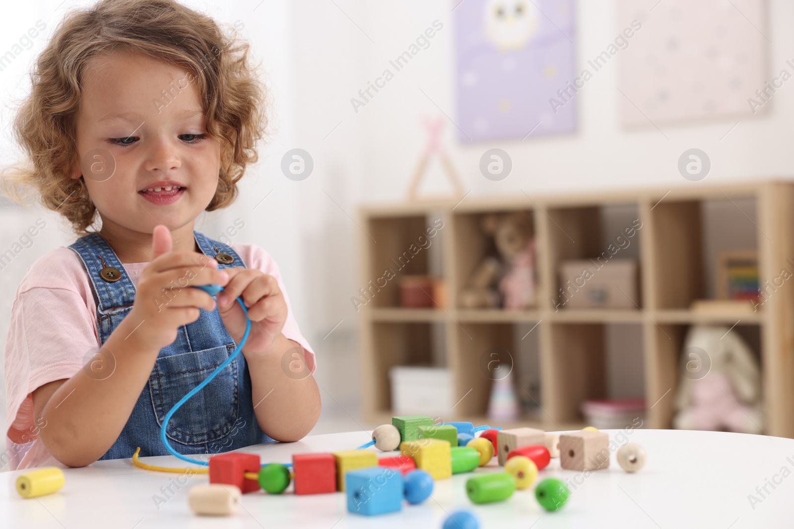 Photo of Motor skills development. Little girl playing with wooden pieces and string for threading activity at table indoors