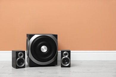 Photo of Modern powerful audio speaker system on floor near orange wall. Space for text