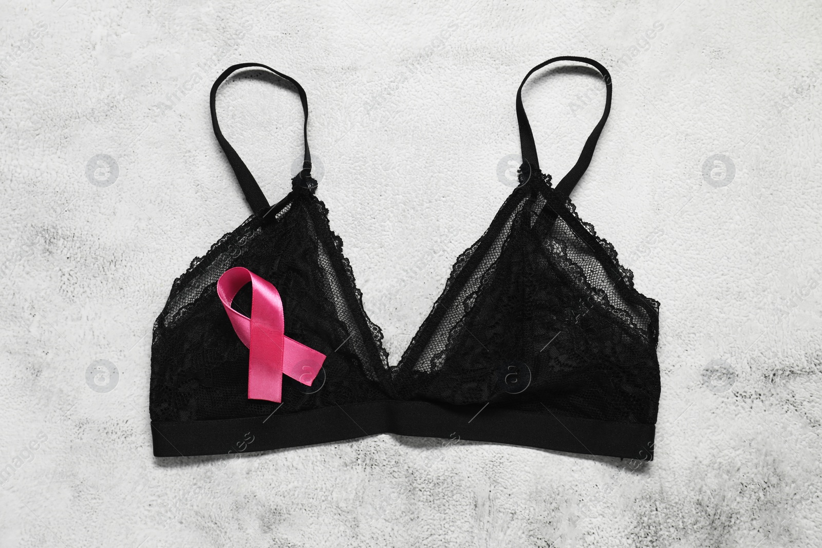 Photo of Pink ribbon and bra on white textured table, top view. Breast cancer awareness