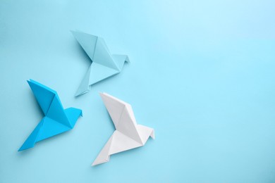 Photo of Origami art. Colorful handmade paper birds on light blue background, flat lay. Space for text