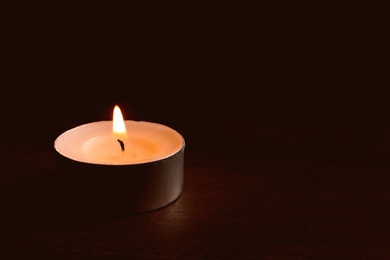 Photo of Wax candle burning on table in darkness