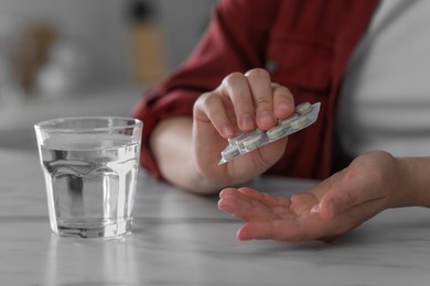 Photo of Woman taking antidepressant pill out from blister near glass of water at white marble table, closeup