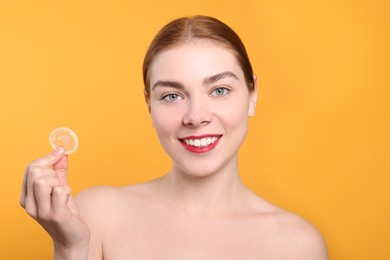 Photo of Woman holding condom on yellow background. Safe sex