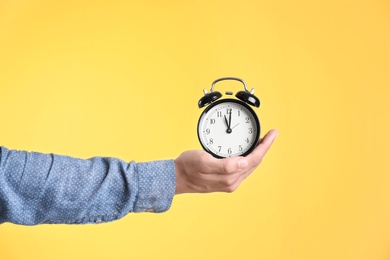 Young man holding clock on color background. Time management