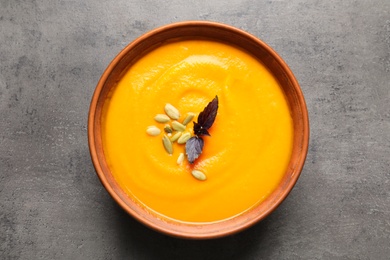 Photo of Bowl with tasty pumpkin soup on gray table, top view