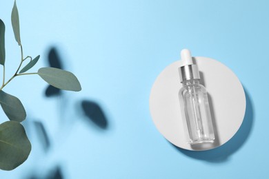 Bottle of cosmetic oil and green leaves on light blue background, top view