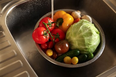 Photo of Washing different vegetables with tap water in metal colander inside sink