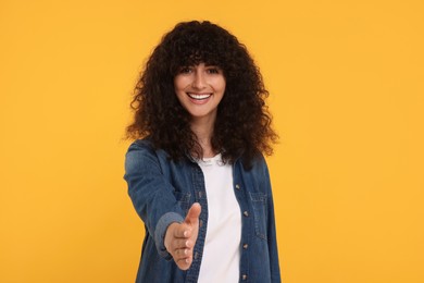 Photo of Happy young woman welcoming and offering handshake on yellow background