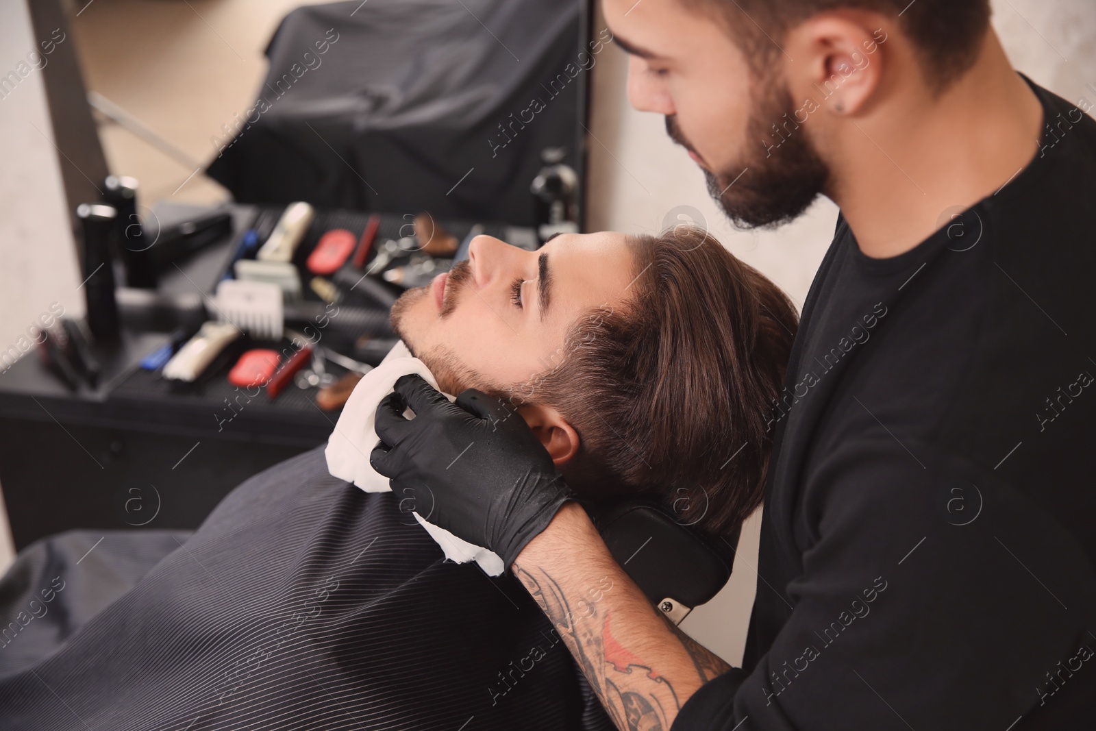 Photo of Professional hairdresser using cold towel to calm client's skin after shaving in barbershop