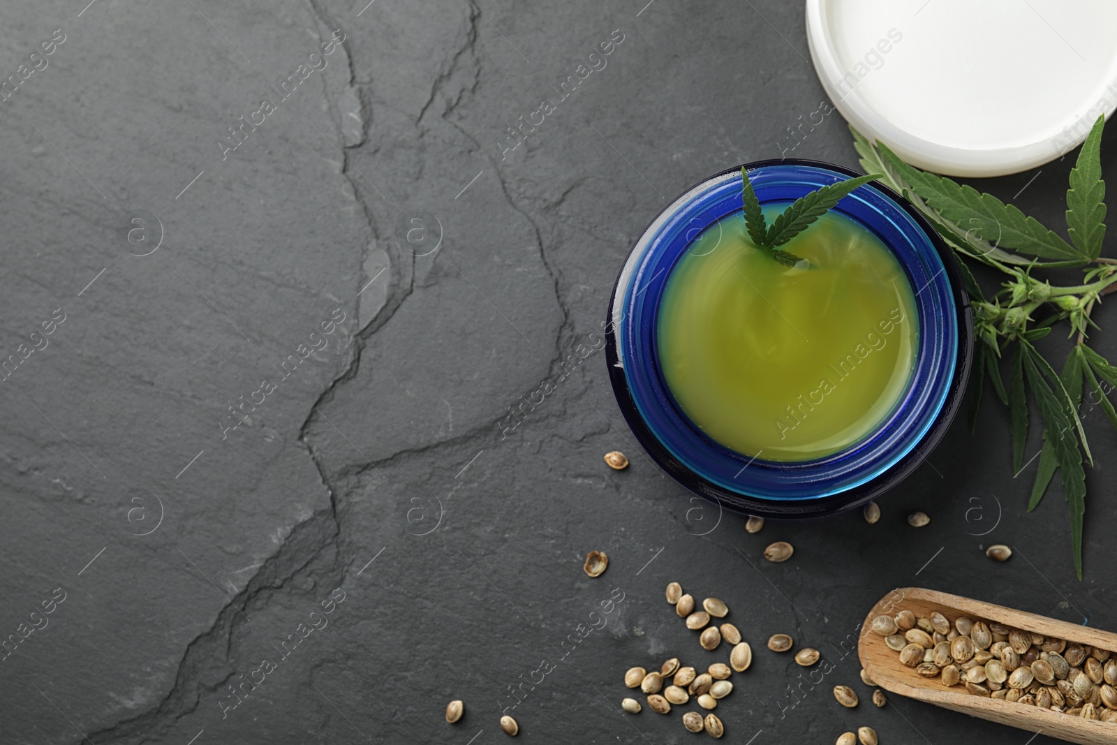 Photo of Jar of hemp cream and seeds on dark stone table, flat lay with space for text. Organic cosmetics