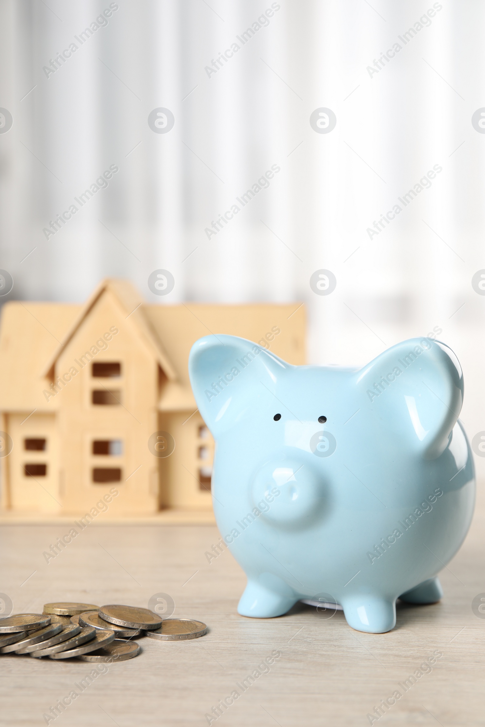 Photo of House model, piggy bank and coins on wooden table indoors, selective focus