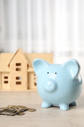 Photo of House model, piggy bank and coins on wooden table indoors, selective focus