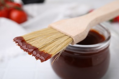 Photo of Marinade in jar and basting brush on white table, closeup