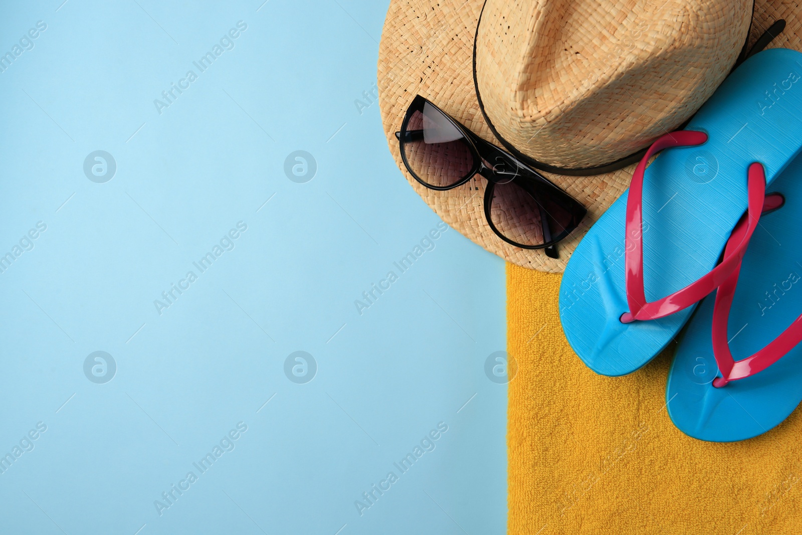 Photo of Flip flops, towel, sunglasses and hat on light blue background, flat lay with space for text. Beach accessories