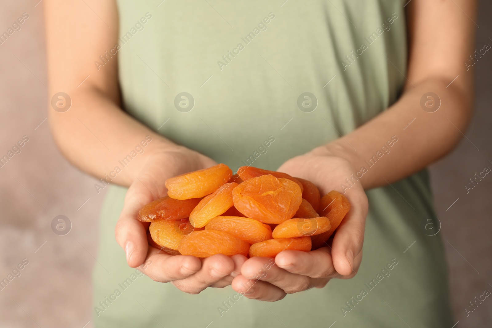 Photo of Woman holding handful of dried apricots on color background, closeup. Healthy fruit