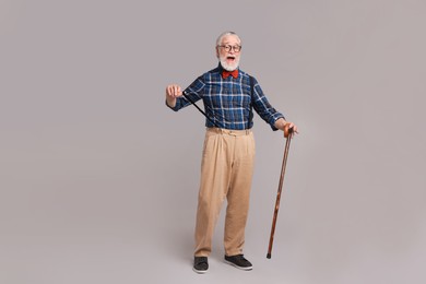 Emotional senior man with walking cane on gray background