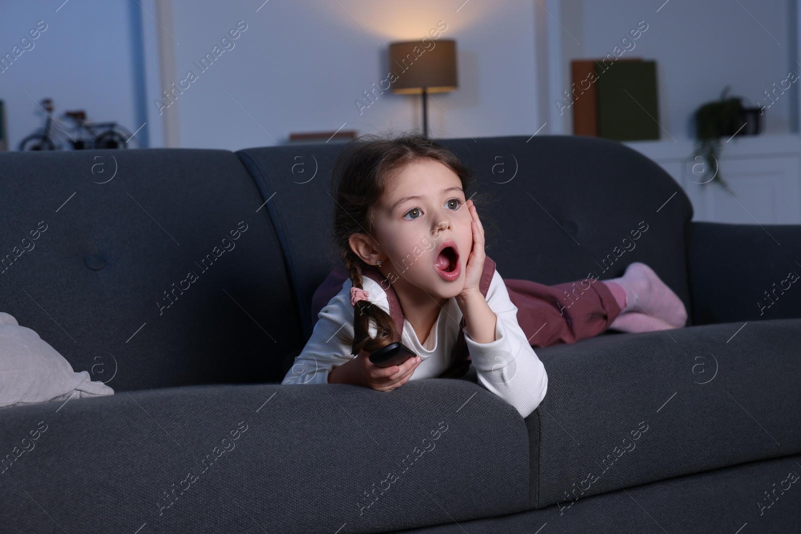 Photo of Shocked girl watching TV on sofa at home