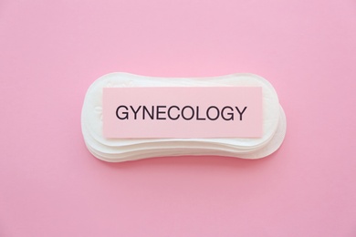 Card with word GYNECOLOGY and menstrual pads on color background, top view. Gynecological care