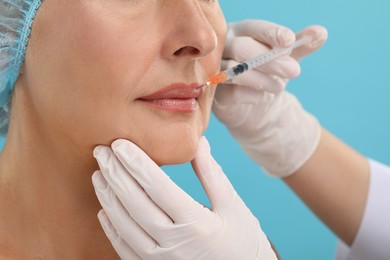 Doctor giving lips injection to senior woman on light blue background, closeup. Cosmetic surgery