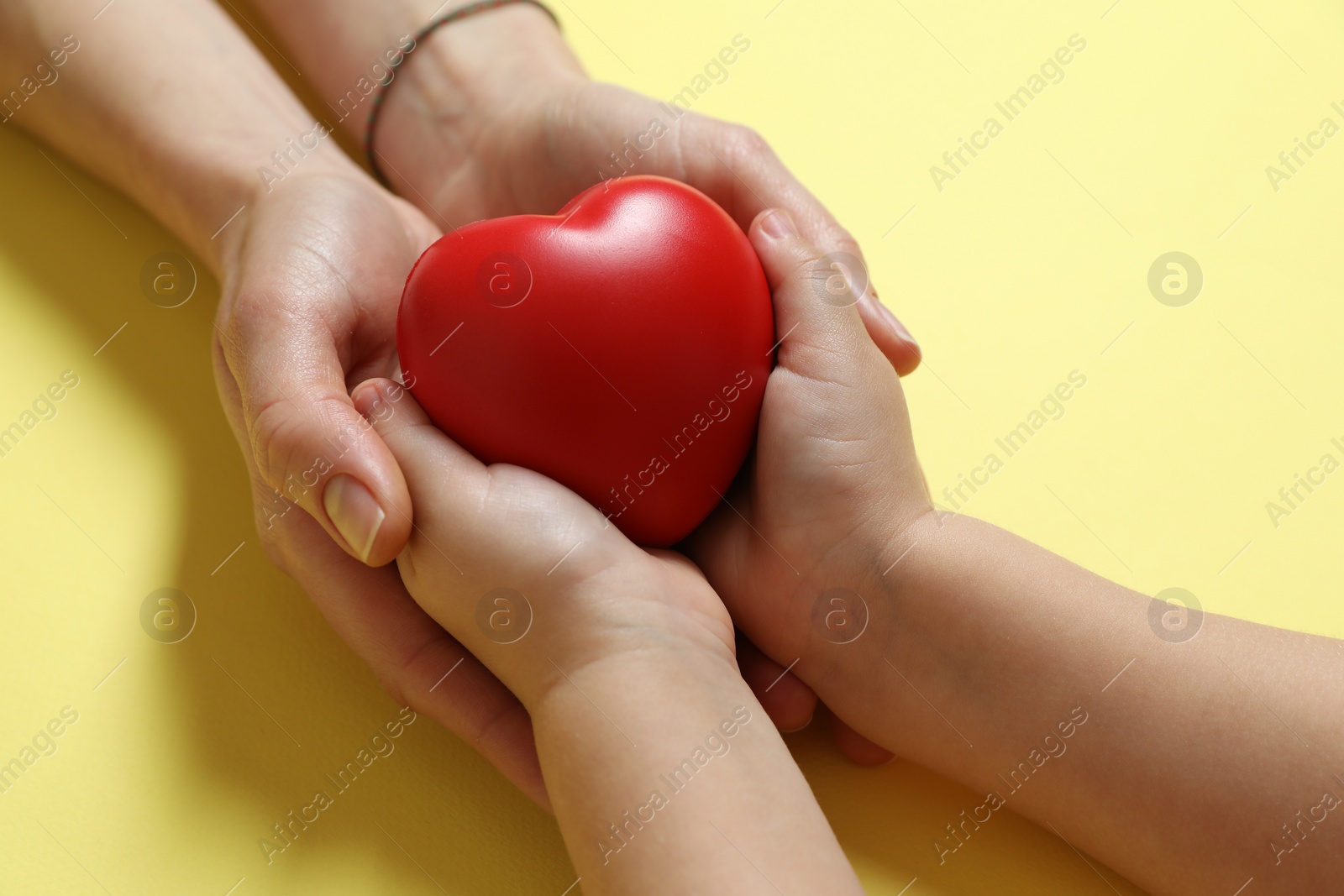 Photo of Mother and her child holding red decorative heart on pale yellow background, closeup