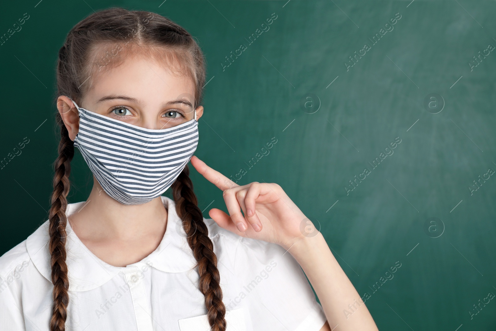 Photo of Schoolgirl wearing protective mask near green chalkboard, space for text. Child's safety from virus