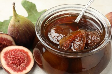 Jar of tasty sweet jam and fresh figs on white table, closeup