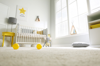 Photo of Cute baby room interior with crib and big window, low angle view