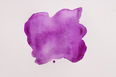 Blot of purple watercolor paint on white paper, top view