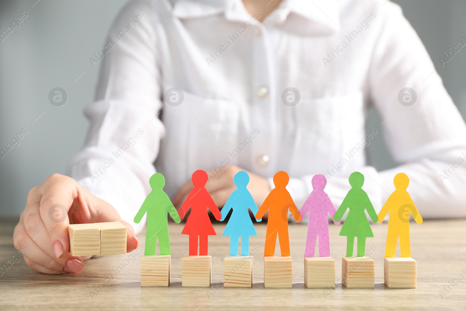 Photo of Woman holding wooden cubes near paper human figures at table indoors, closeup. Diversity and Inclusion concept