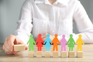 Photo of Woman holding wooden cubes near paper human figures at table indoors, closeup. Diversity and Inclusion concept