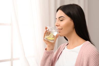 Photo of Beautiful young woman drinking fresh lemon water indoors. Space for text