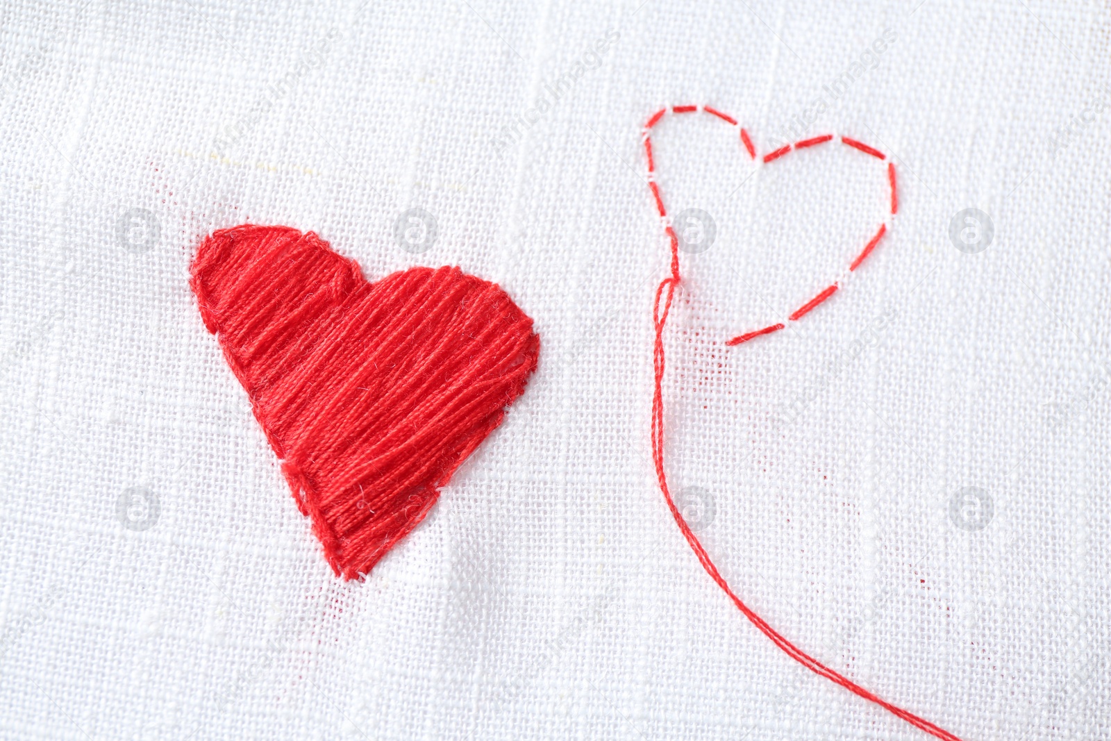 Photo of Embroidered red hearts and needle on white cloth, top view