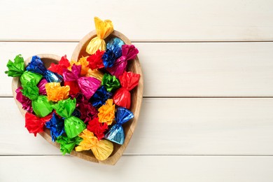 Photo of Candies in colorful wrappers on beige wooden table, top view. Space for text