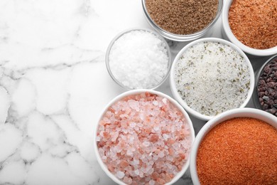 Different kinds of salt on white marble table, flat lay. Space for text