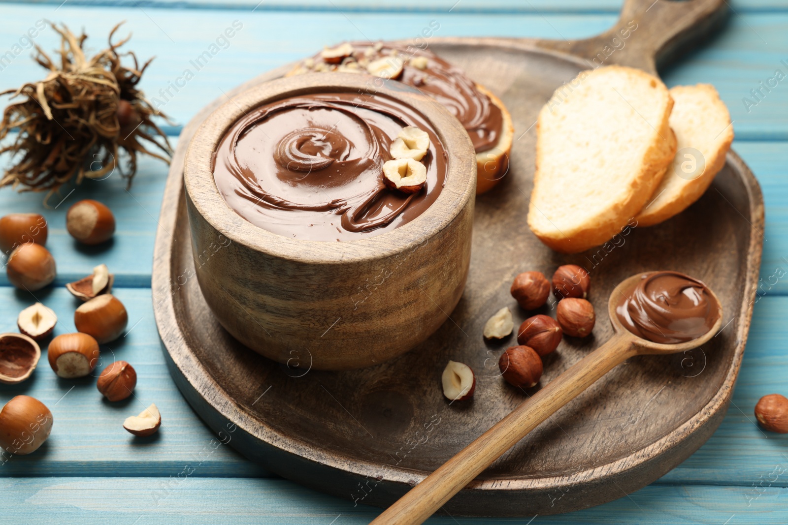 Photo of Bowl of tasty chocolate paste with hazelnuts on light blue wooden table