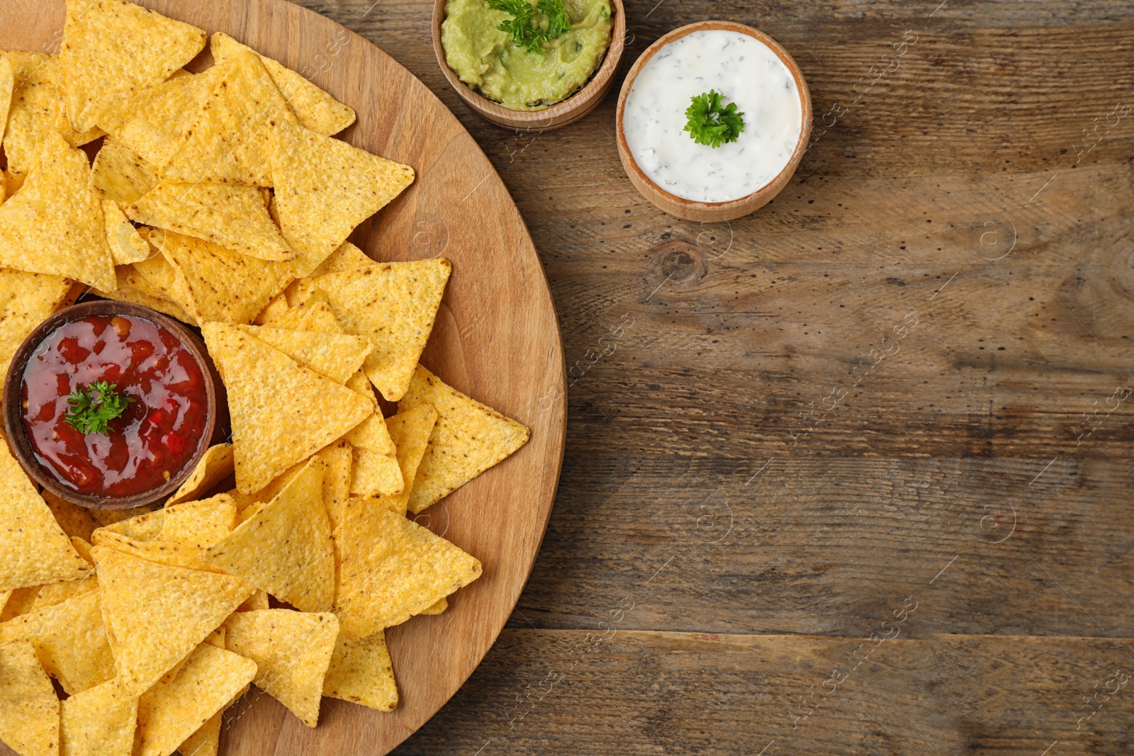 Photo of Mexican nacho chips with different sauces on wooden background, flat lay. Space for text