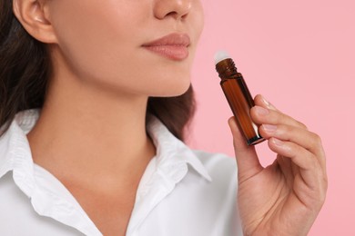 Woman with roller bottle of essential oil on pink background, closeup