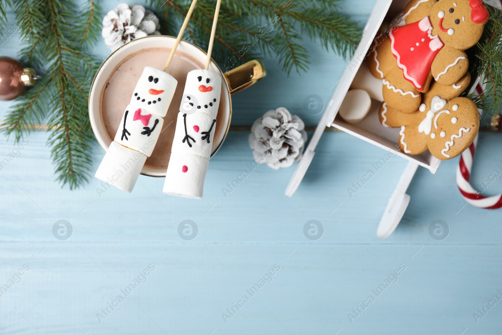 Photo of Flat lay composition with funny snowmen made of marshmallows on light blue wooden table. Space for text