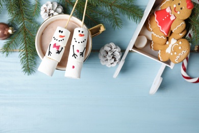 Photo of Flat lay composition with funny snowmen made of marshmallows on light blue wooden table. Space for text