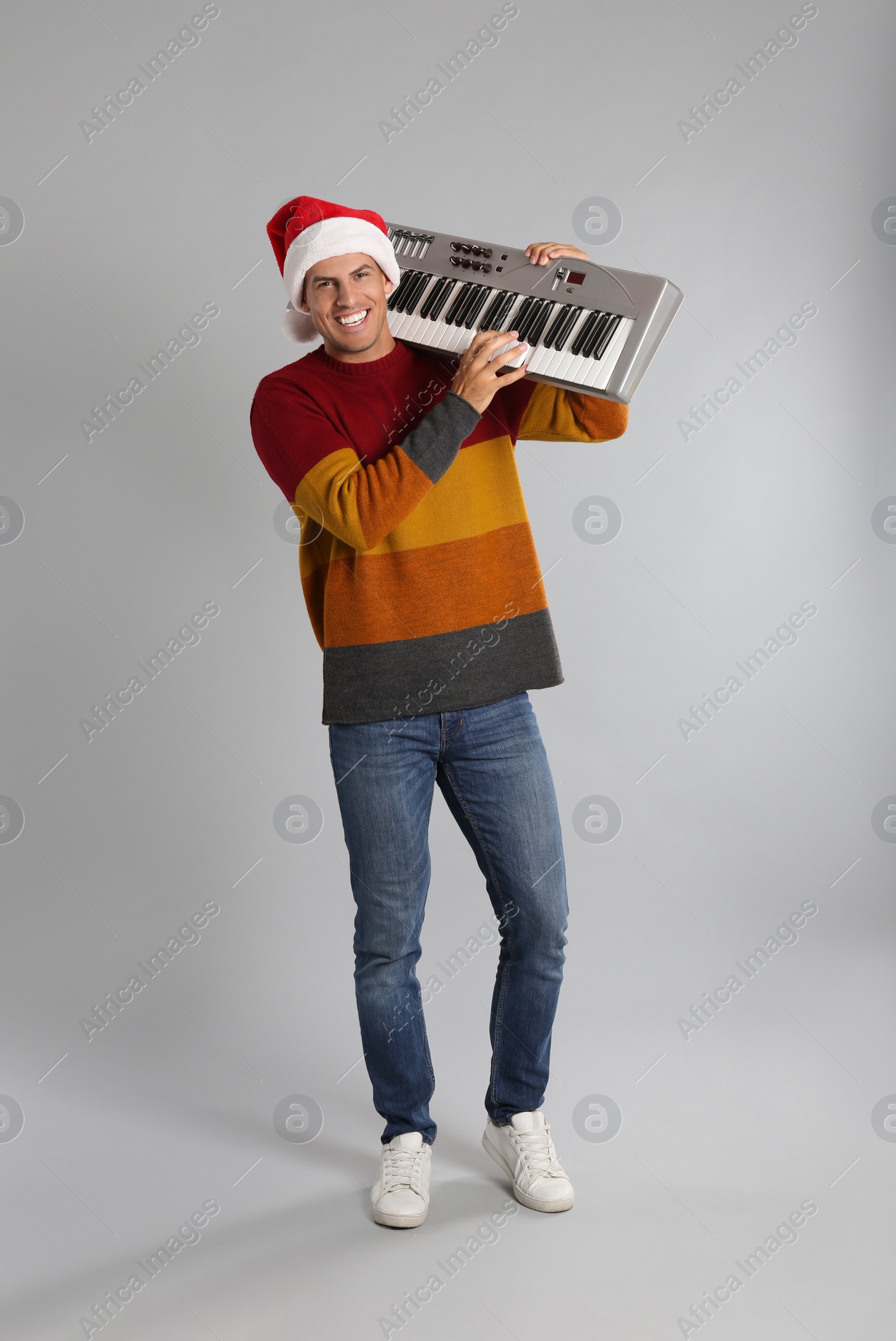 Photo of Man in Santa hat playing synthesizer on light grey background. Christmas music